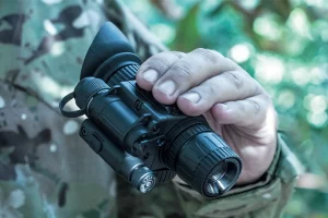 Soldier holding NVMA monocular night vision device in field camouflage uniform